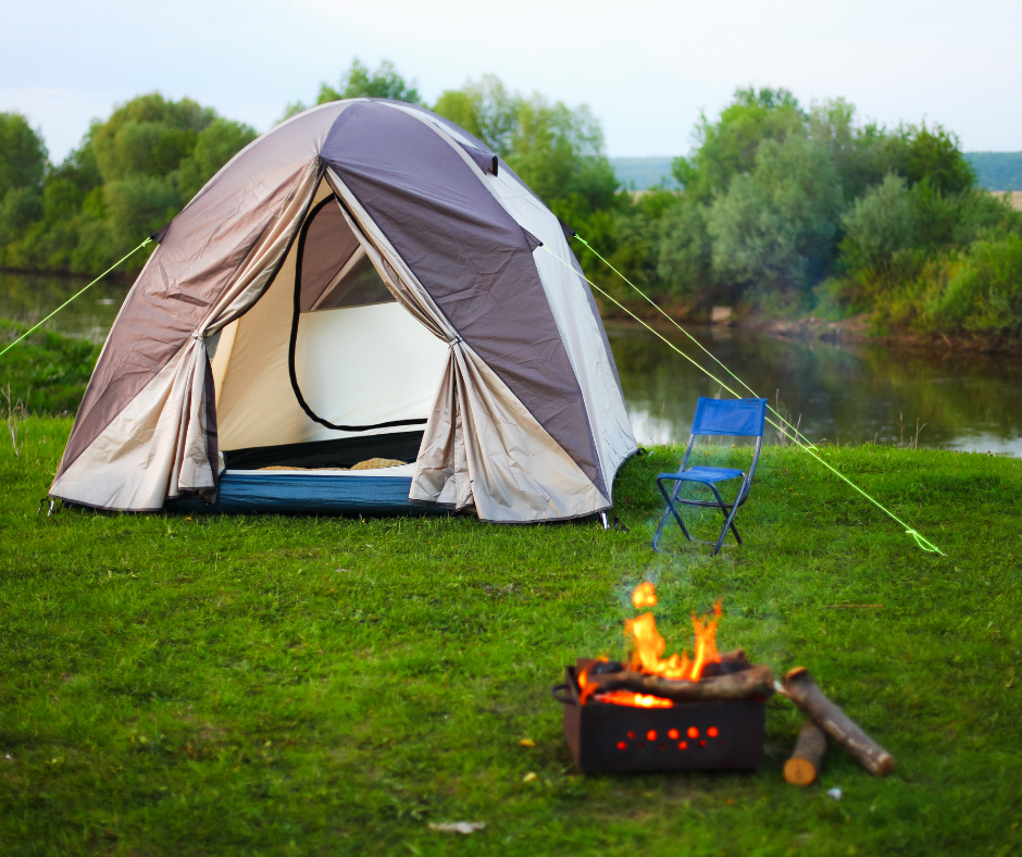 Open tent next to a fire with a small pond in the background.