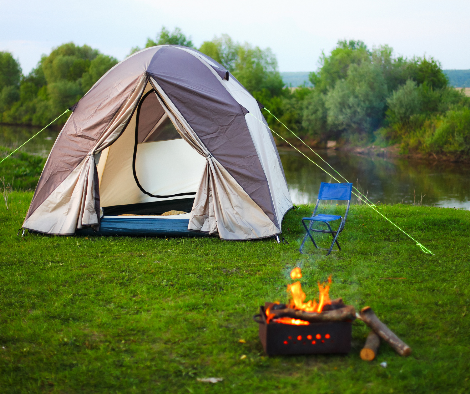 Open tent next to a fire with a small pond in the background. 